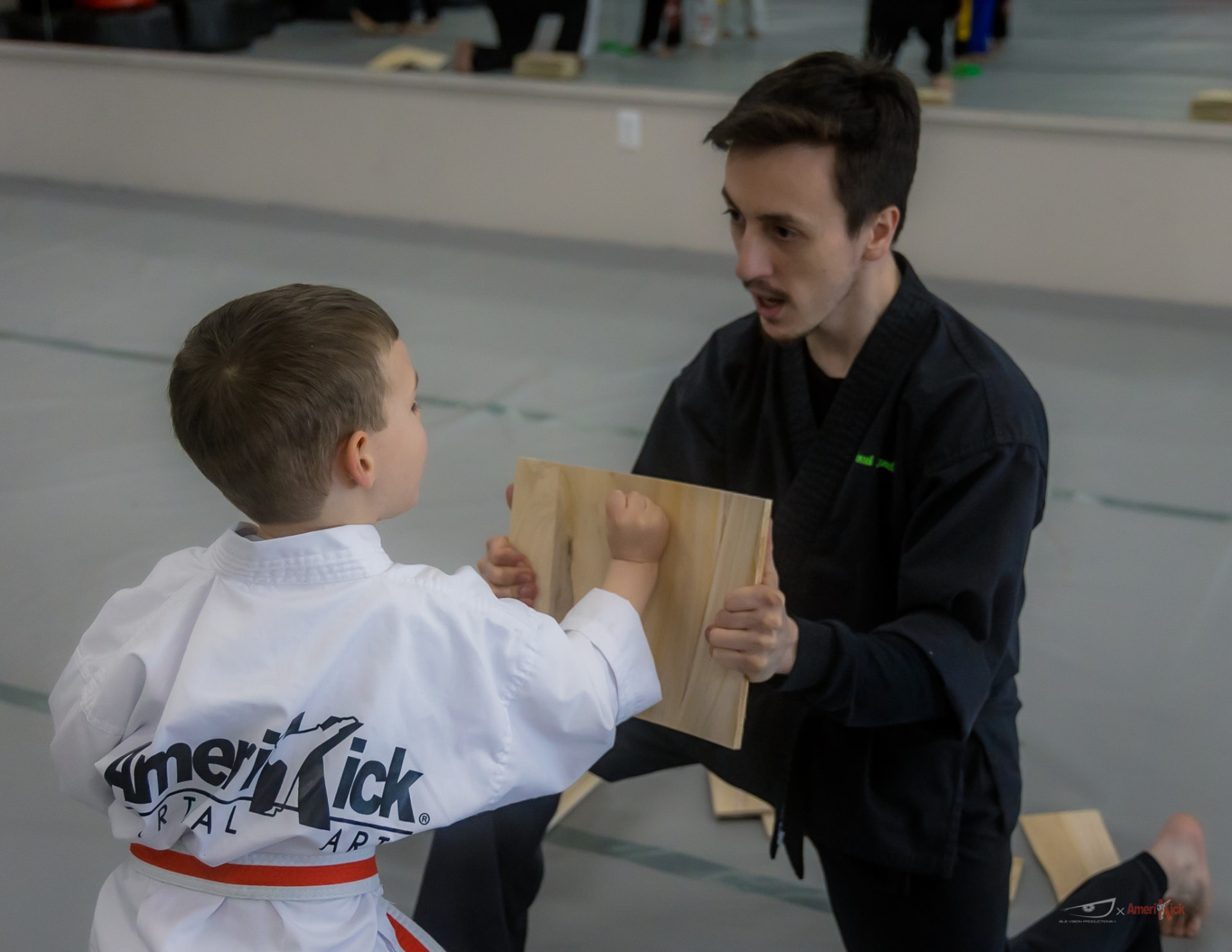 A young student in a white gi punching through a board held by an instructor